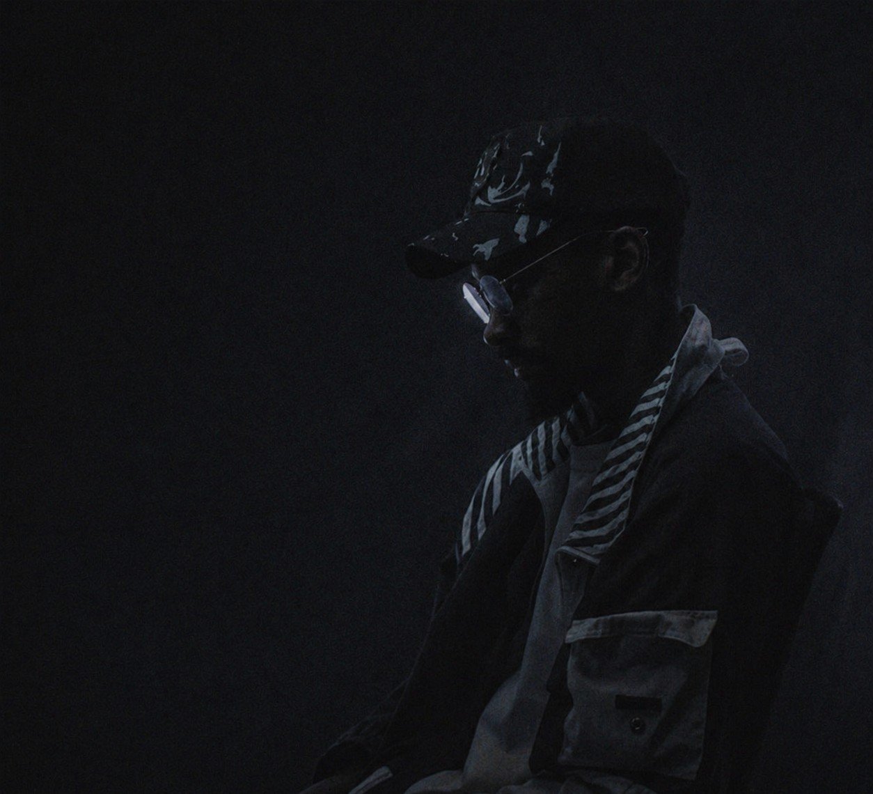 Den Creus seated in shadow, wearing a cap and glasses